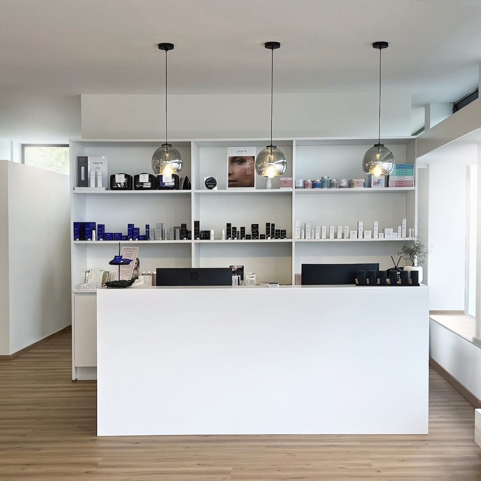 Empfangsbereich im Beautyloft mit hellem Tresen, Produktregal und Pendelleuchten