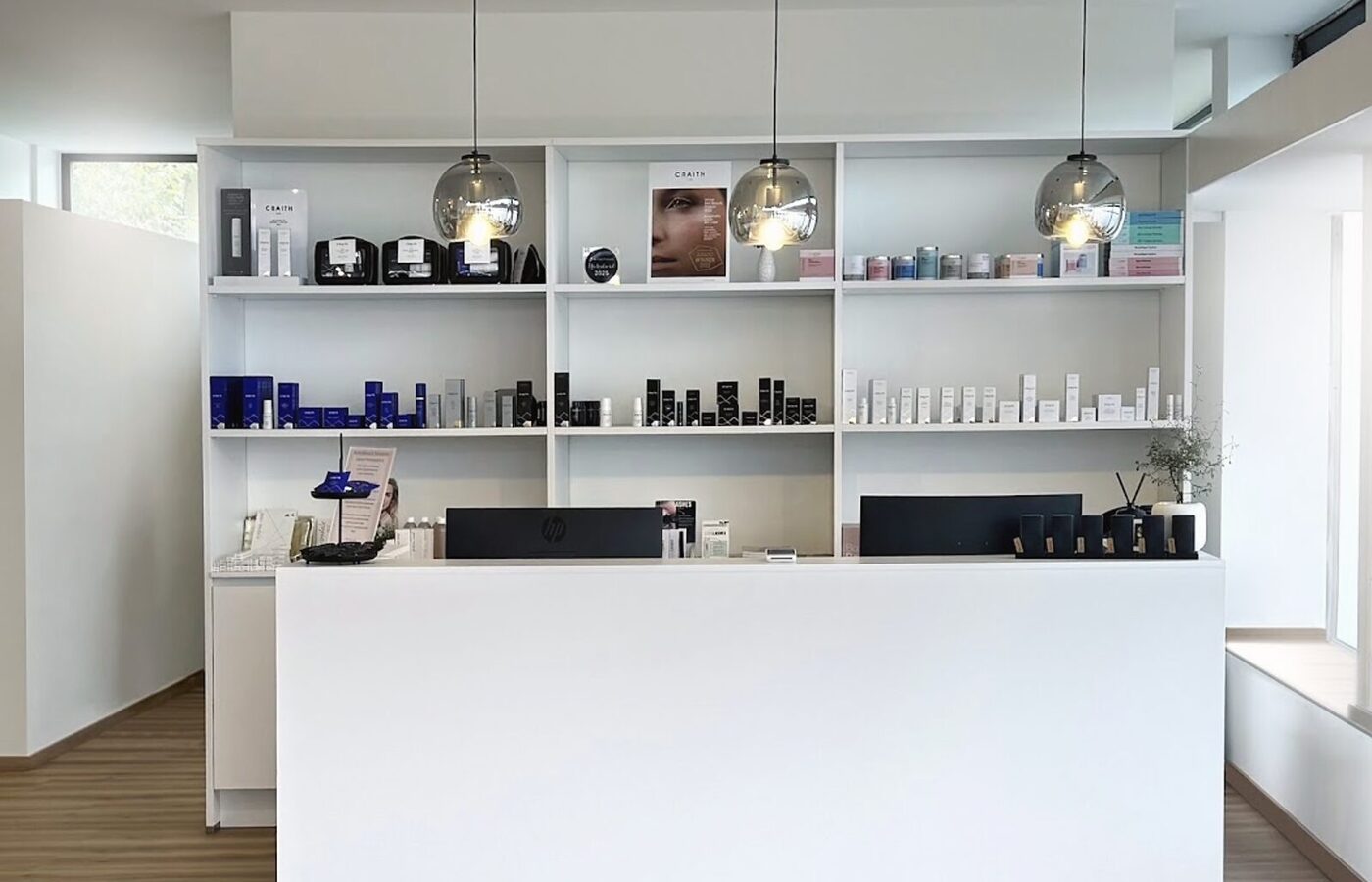 Empfang im Beautyloft: heller Tresen vor dem weißen Regal mit Craith-Lab- und Comfort-Zone-Produkten, darüber drei Glaspendelleuchten